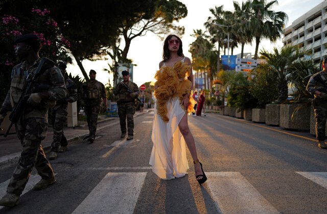 Topshot - A woman stands next to French soldiers of the Sentinelle security operation on the sidelines of the 77th edition of the Cannes Film Festival at the Boulevard de la Croisette in Cannes, southern France, on May 22, 2024. (Photo by VALERIE HACHE/AFP) (Photo by VALERIE HACHE/AFP via Getty Images)